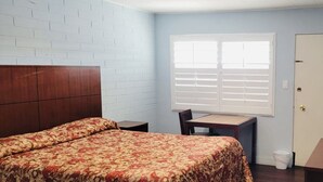 A bedroom with a bed, a desk, a chair, a TV, and a door. - Wiebe Motel (Hollister)