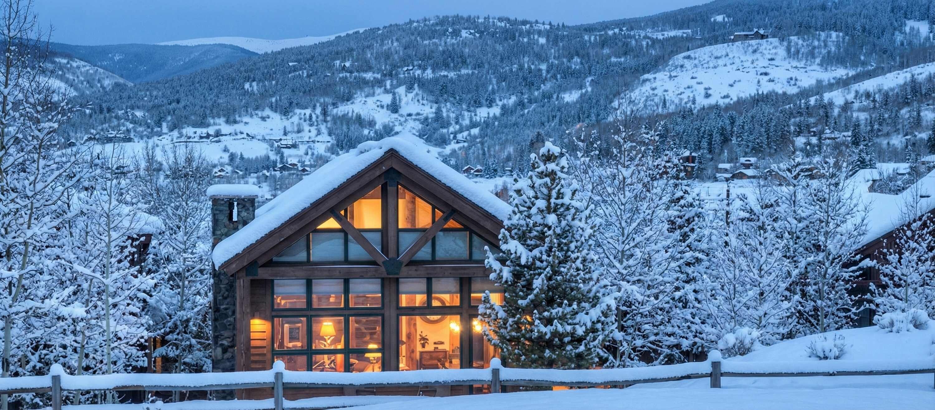 Une cabane en bois dotée d’une grande fenêtre, entourée d’arbres et de montagnes couverts de neige.