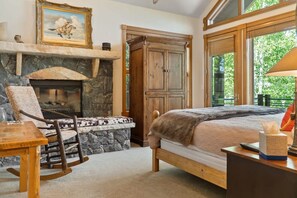 Une chambre dotée d’une cheminée en pierre, d’une armoire en bois et d’un lit offrant une vue sur la verdure environnante.