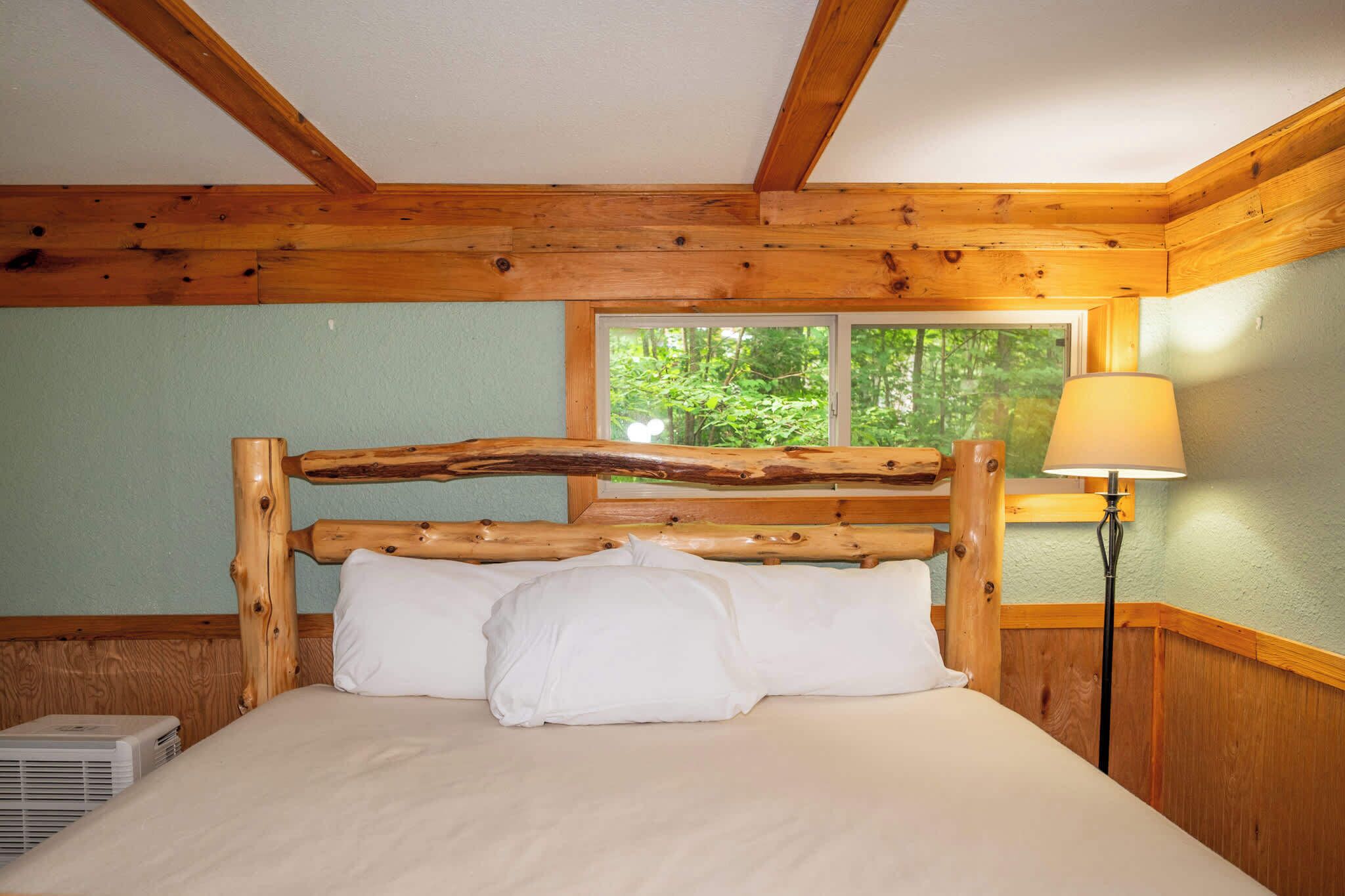 A wooden bed with a slatted headboard in a room with a window and a lamp.
