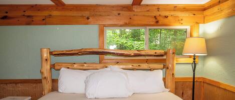 A wooden bed with a slatted headboard in a room with a window and a lamp.
