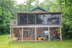 Une cabane à deux étages dotée d’un balcon, d’une terrasse en bois et d’une pile de bois de chauffage.