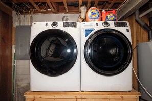 Deux machines à laver à chargement frontal, posées sur une plateforme en bois, avec des bouteilles de lessive Tide placées au-dessus.