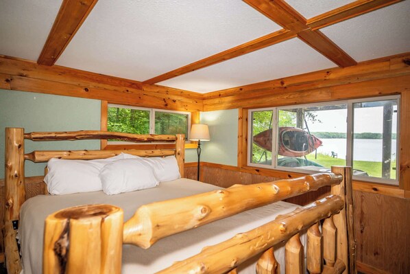 A wooden cabin bedroom with a bed, windows, and a view of a lake.