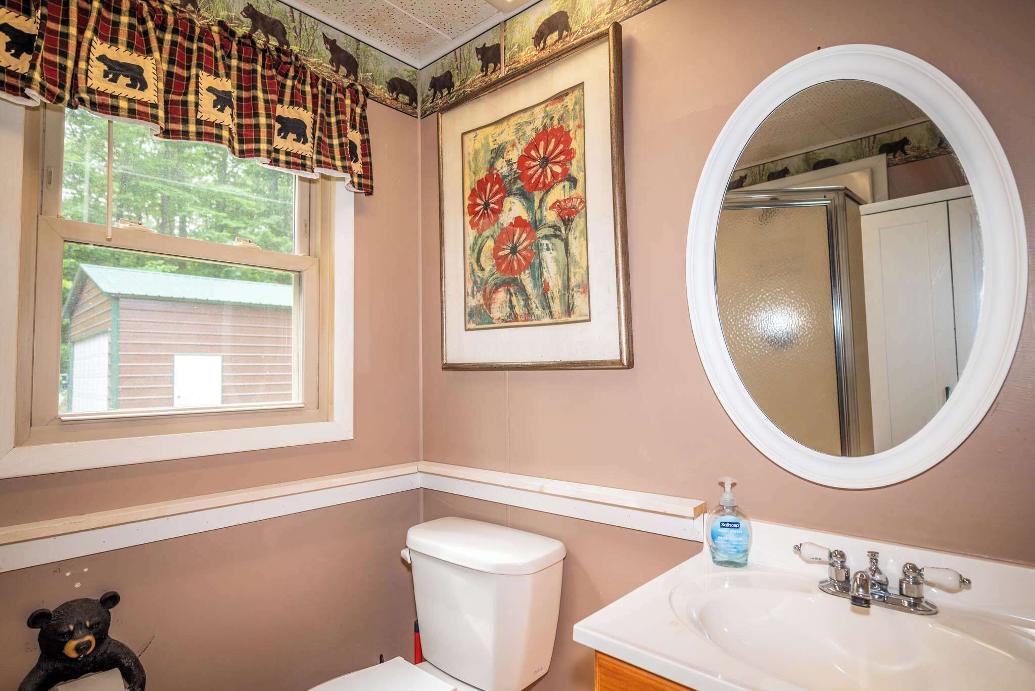 Une salle de bain comprenant des toilettes, un lavabo, un miroir, une fenêtre avec des rideaux à carreaux et une décoration murale sur le thème des ours.
