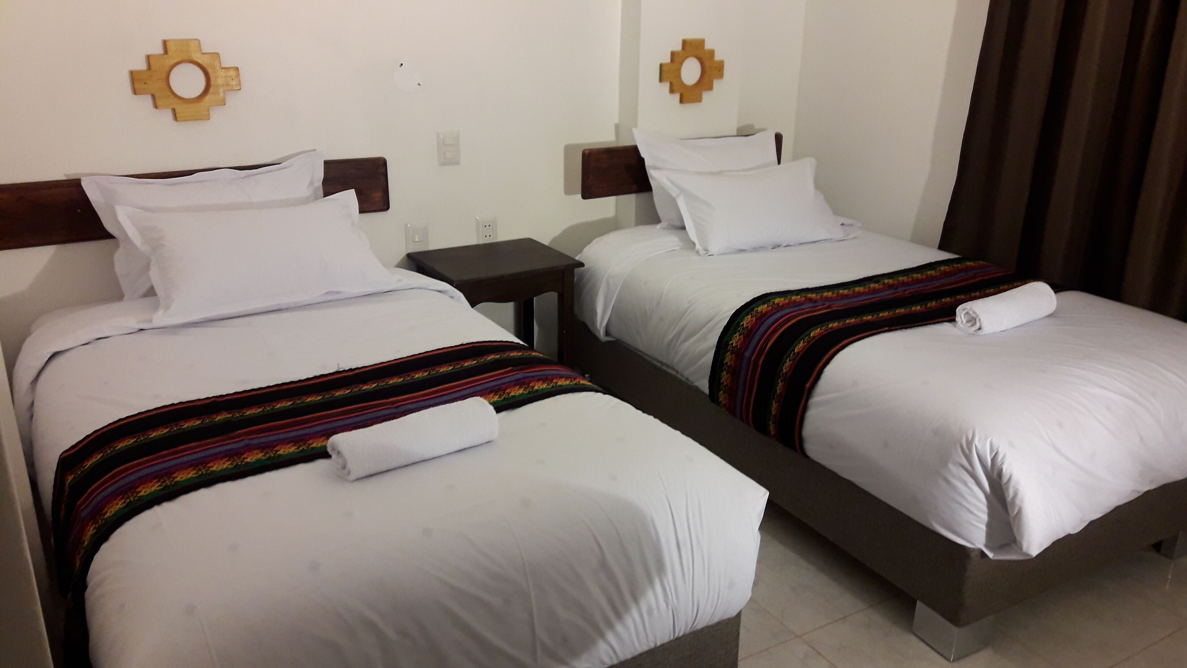 Two twin beds with white linens and colorful blankets, wooden headboards, and small bedside tables.