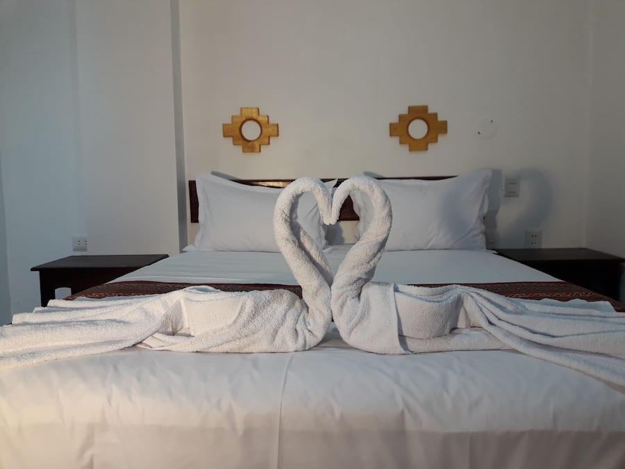 Cama com lençóis brancos e duas toalhas dispostas em formato de coração na cama.