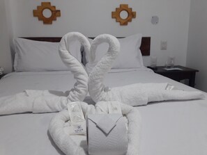 A neatly made bed with white linens and two towels arranged in a heart shape. - Pakarina Hotel  (Machu Picchu)