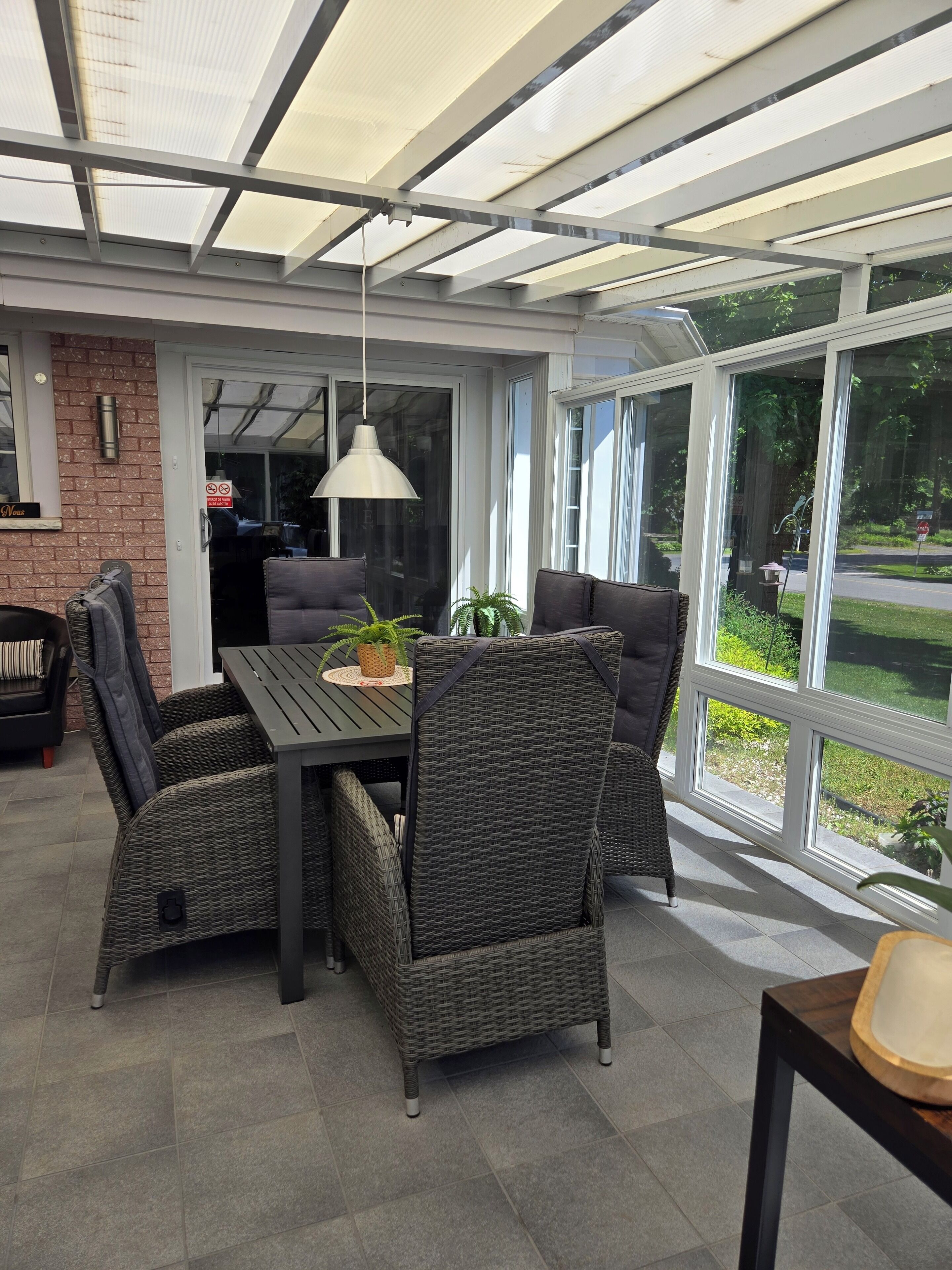 A covered patio area with a table and chairs, large windows, and a hanging light fixture.