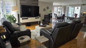A modern living room with a flat-screen TV, leather sofas, a coffee table, and a dining area with chairs and a table. - La Maison du Bonheur 🫶 (Saint-Paul-d'Abbotsford)
