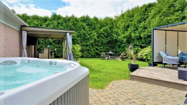 A hot tub in a backyard with a patio area and outdoor furniture. - La Maison du Bonheur 🫶 (Saint-Paul-d'Abbotsford)
