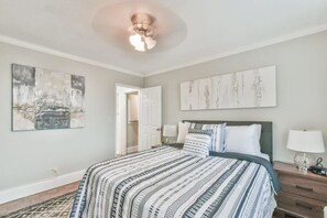 Quarto com uma cama grande, duas mesas de cabeceira com luminárias, um ventilador de teto e obras de arte nas paredes.