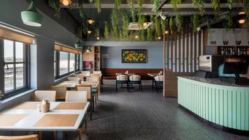 A restaurant interior with tables, chairs, hanging plants, a counter, and a menu board.
