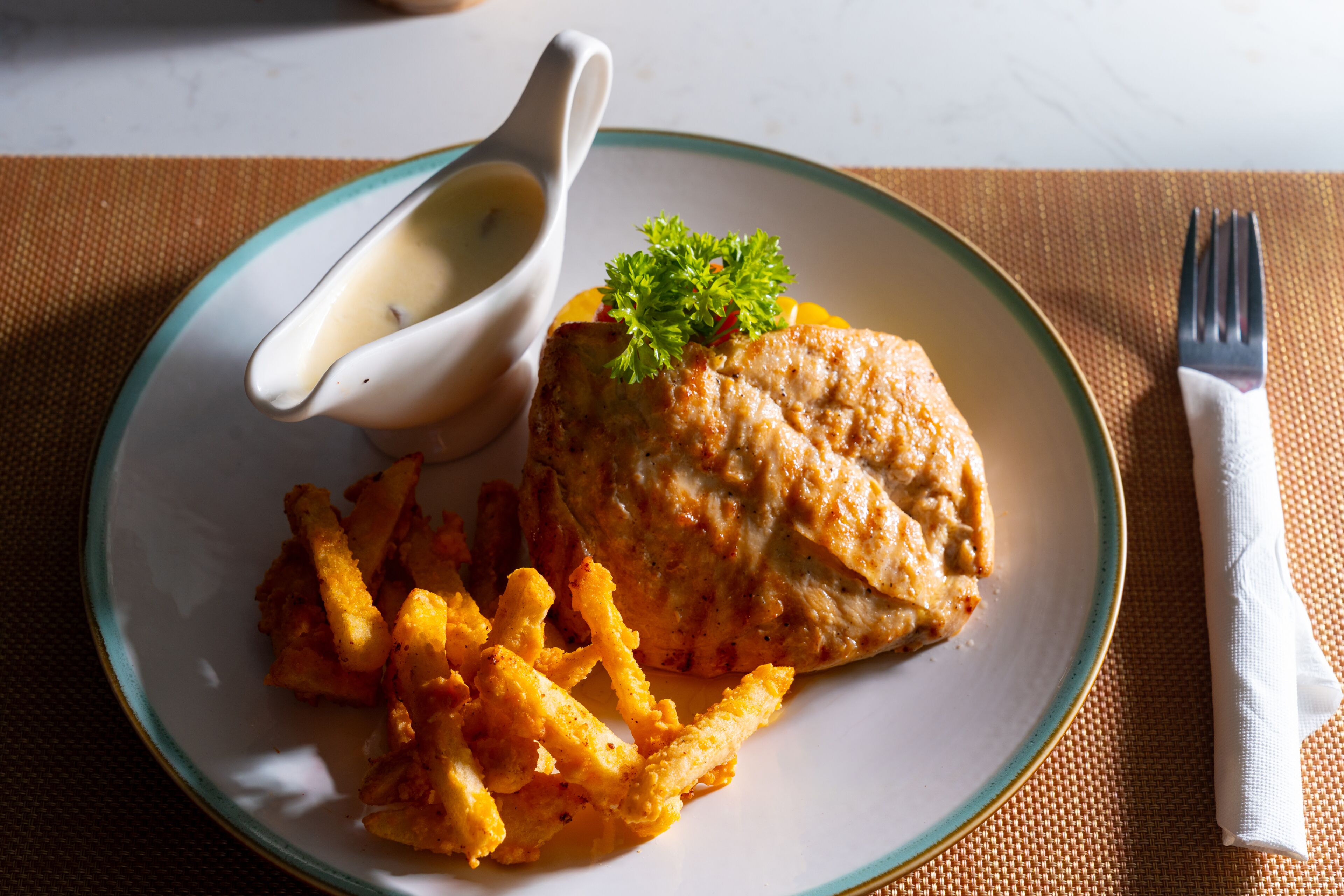 Une assiette contenant une escalope de poulet panée, des frites et un petit bol de sauce.