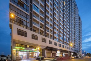 Un hotel de altura con varios pisos, balcones y un área comercial en la planta baja con tiendas y una tienda de conveniencia.