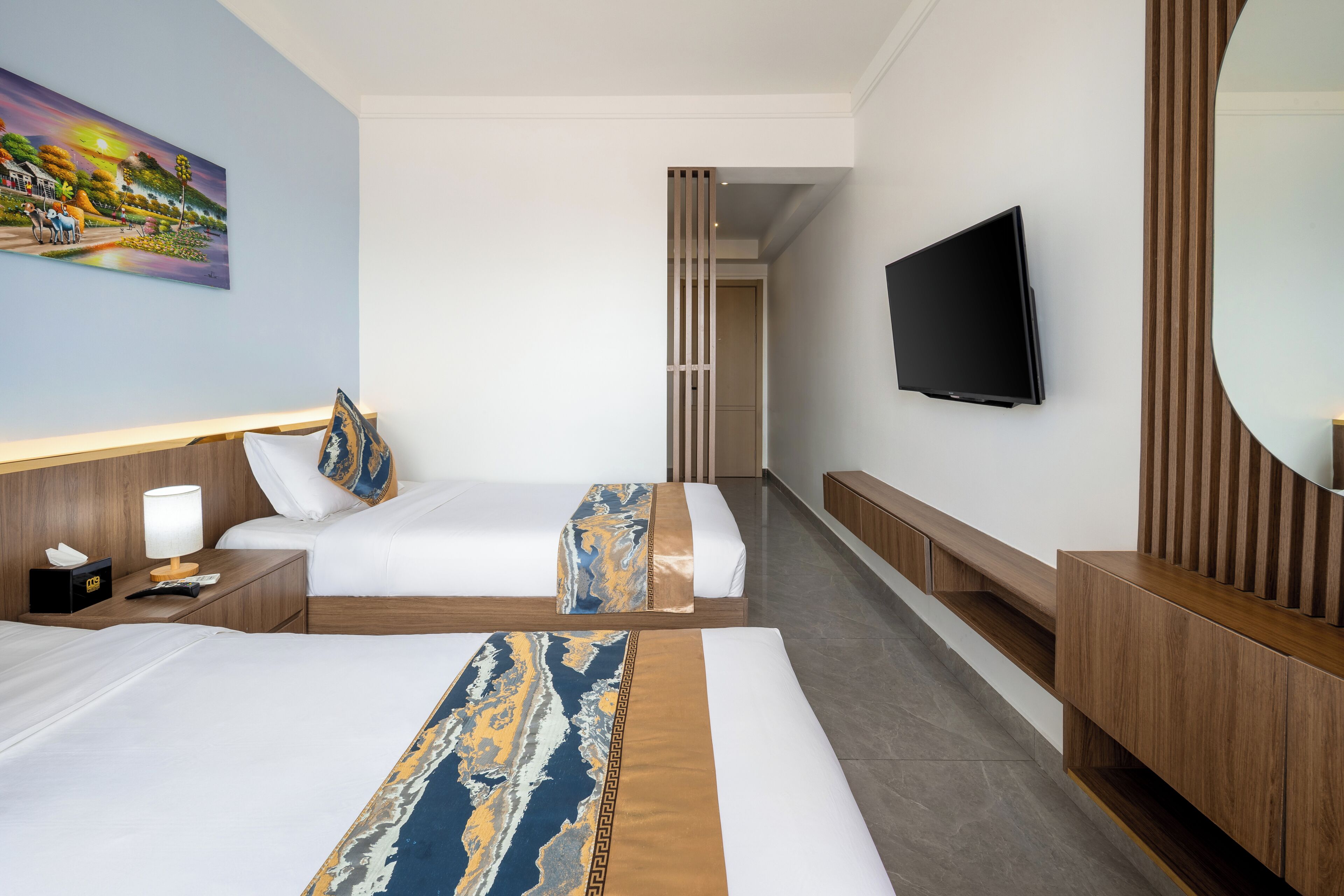 A hotel room with two beds, a television, a painting, and a wooden bench.
