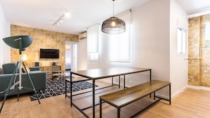 Una sala moderna con piso de madera, un sofá verde, una lámpara de pie negra, una mesa de comedor con bancos y una lámpara colgante grande.