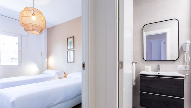 Una habitación de hotel con cama, mesita de noche y baño con lavamanos y espejo.