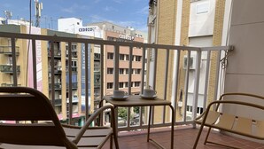 A balcony with two chairs and a small table, overlooking a cityscape with buildings labeled 'CEDECO'. - Apartamento con Terraza y Parking Gratis (Sevilla)