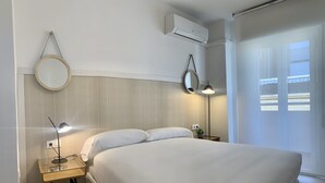A modern hotel room with a large bed, two bedside tables with lamps, a round mirror, and an air conditioning unit. - Apartamento con Terraza y Parking Gratis (Sevilla)