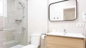 Ein modernes Badezimmer mit einer Glaskabine zur Dusche, einer weißen Toilette, einem hölzernen Waschtisch mit Waschbecken und einem Spiegel darüber.