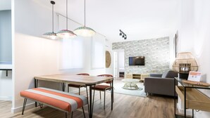 Ein modernes Wohnzimmer mit einem Holzespeisetisch, einer orangefarbenen gepolsterten Bank und einem grauen Sofa.