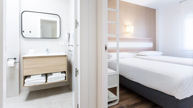 Ein Hotelzimmer mit einem hölzernen Schminktisch, einem Spiegel, einem Nachttisch, einer Lampe und einem Bett mit weißer Bettwäsche.