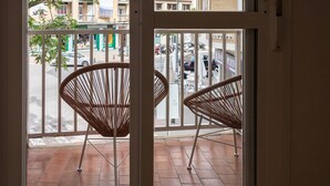Een balkon met twee rieten stoelen en uitzicht op de straat, met een gebouw waarop het bord 'JUPITER' staat.