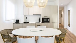 Een moderne keuken met witte kastjes, een ronde eettafel, rieten stoelen en hanglampen.