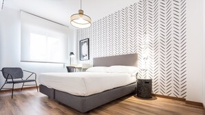 Un dormitorio moderno con una cama, una silla, un cesto de basura y una ventana.