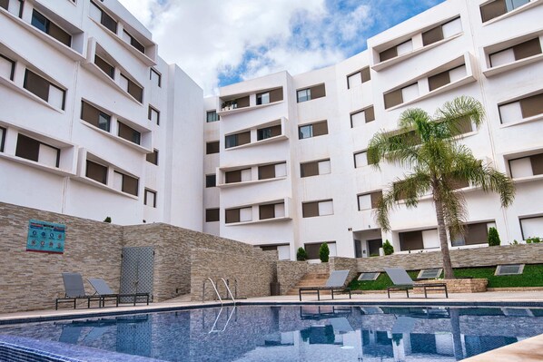 Un bâtiment moderne doté d’une piscine, de nombreux balcons et de chaises longues.
