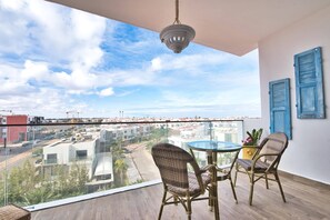 A balcony with wicker chairs, a glass table, and a hanging light fixture. - Appartement Luxueux Avec 2 Piscines, Wi-fi Illimité, Près de la Plage (Agadir)