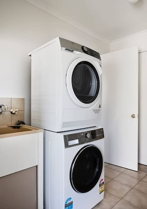 A stacked washer and dryer unit in a room with a beige tiled floor and a white door.
