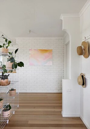 Ein Zimmer mit weißer Ziegelwand, Holzboden, einem rosa abstrakten Gemälde und einem Schuhregal mit Hüten.