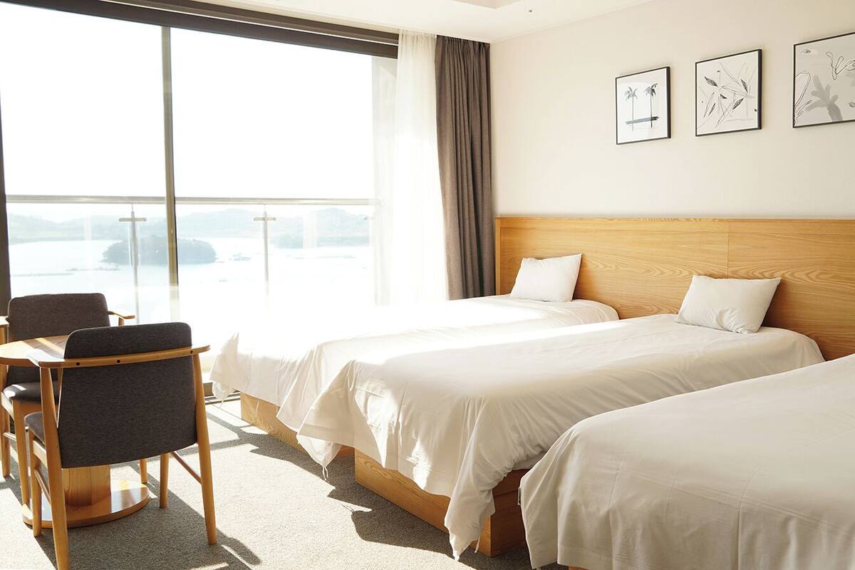 A hotel room with two beds, a desk, and a chair. There are three framed pictures on the wall.