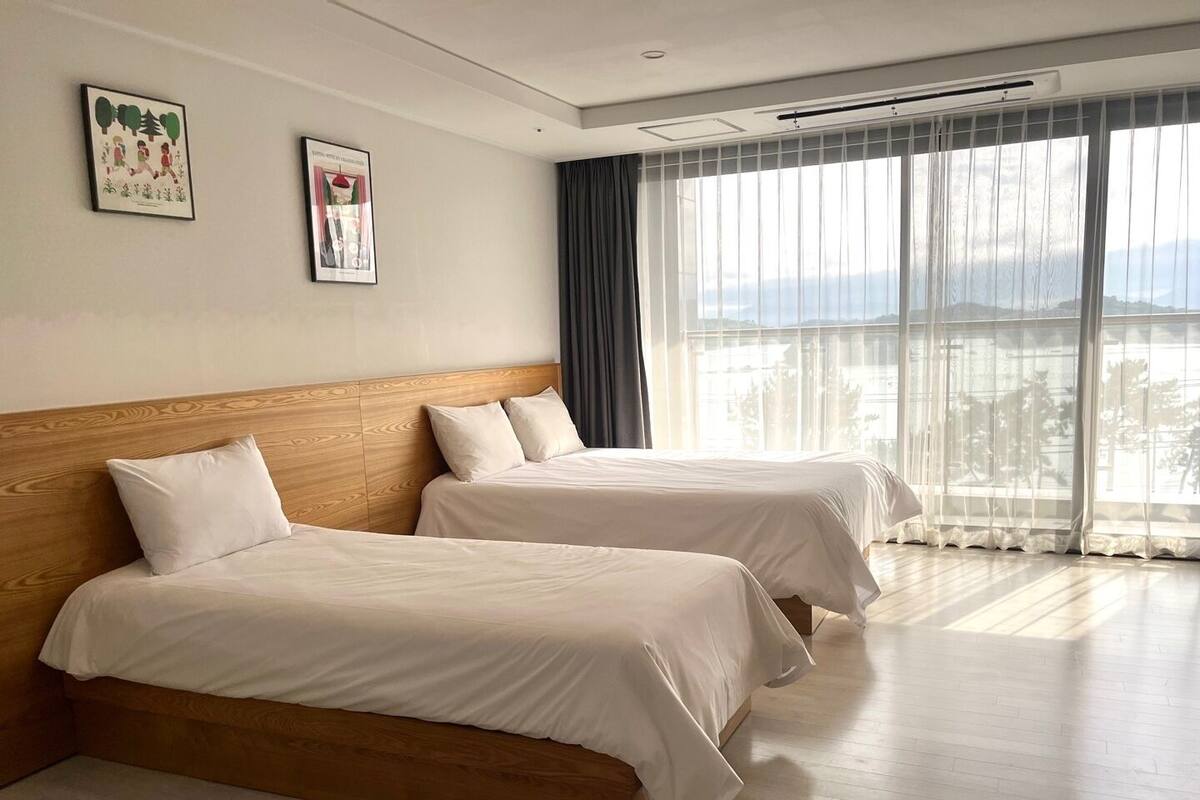 A hotel room with two beds, a large window with curtains, and artwork on the wall.