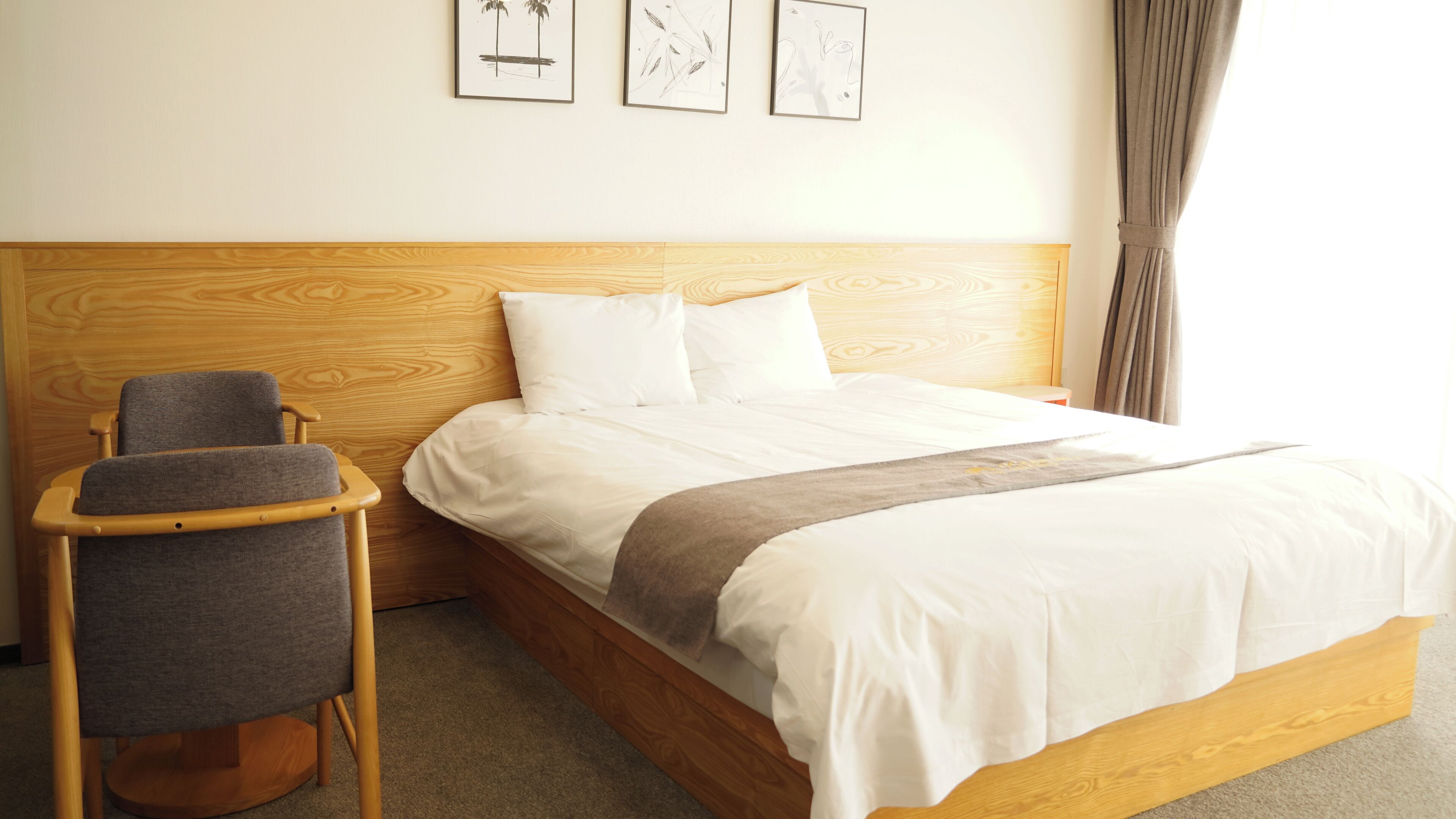 Una cama bien hecha con sábanas blancas, cabecera de madera y una silla gris con reposabrazos.