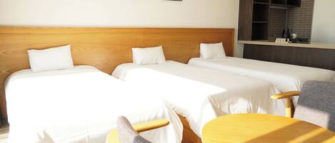A hotel room with two beds, a wooden headboard, a small table, and a kitchenette area.