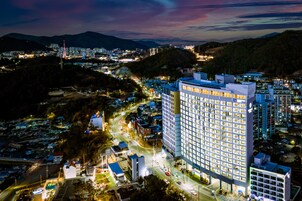 Un hotel moderno de gran altura con varios pisos, rodeado por un paisaje urbano con calles y otros edificios.
