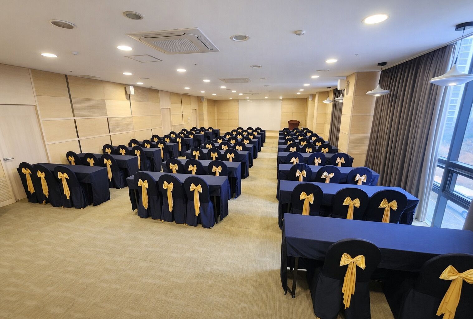 Un salón de conferencias con filas de mesas y sillas, cada una adornada con un lazo en el respaldo.