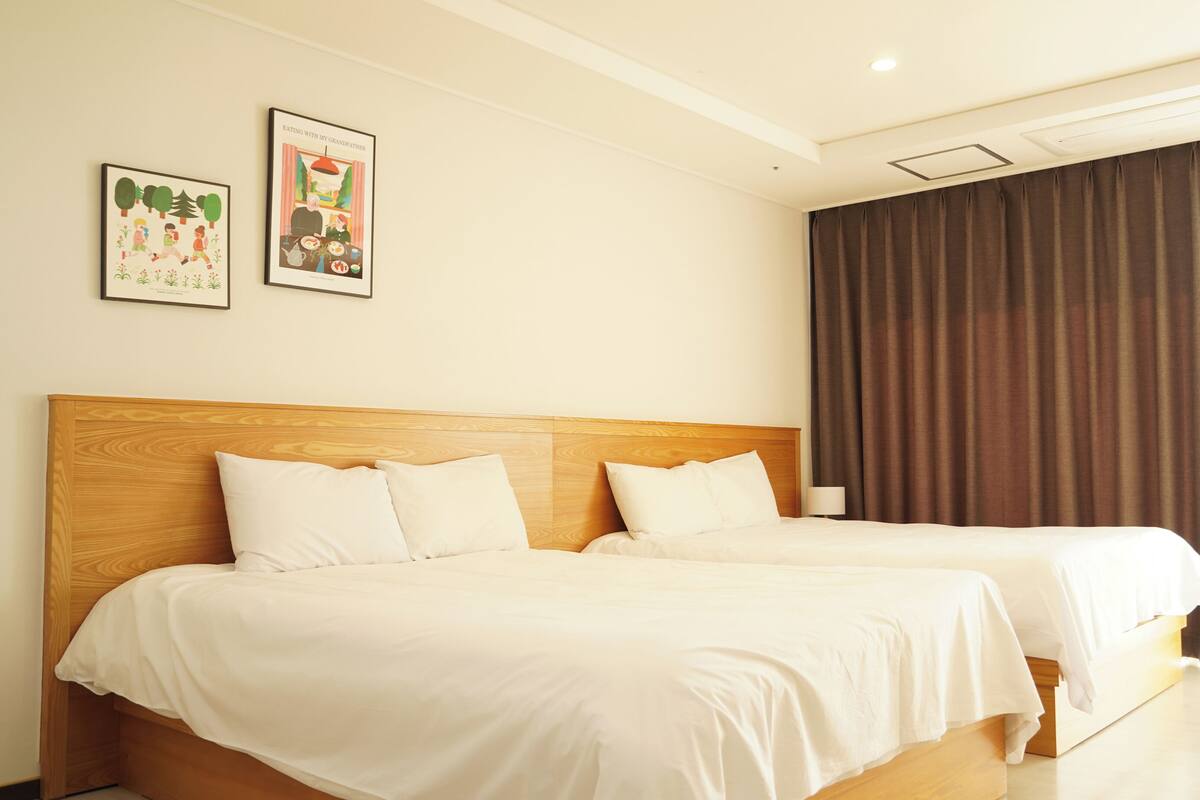 A hotel room with two beds, a wooden headboard, and two framed pictures on the wall.
