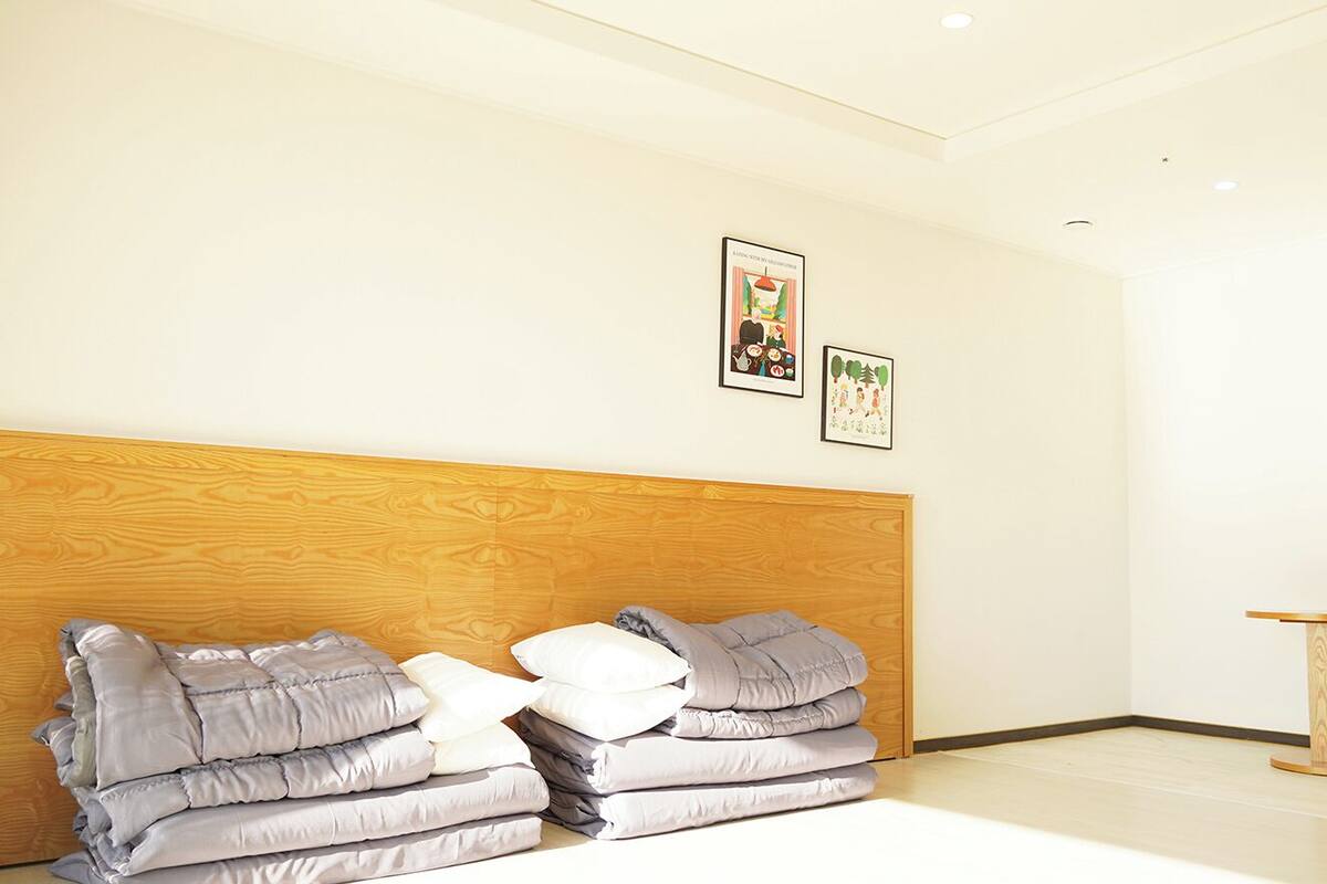 A hotel room with a wooden headboard, a bed with grey and white bedding, a small round wooden table, and two framed pictures on the wall.