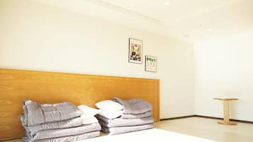 Habitación de hotel con cabecera de madera, cama con ropa de cama gris y blanca, una mesita redonda de madera y dos cuadros enmarcados en la pared.