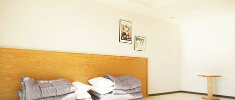 A hotel room with a wooden headboard, a bed with grey and white bedding, a small round wooden table, and two framed pictures on the wall.