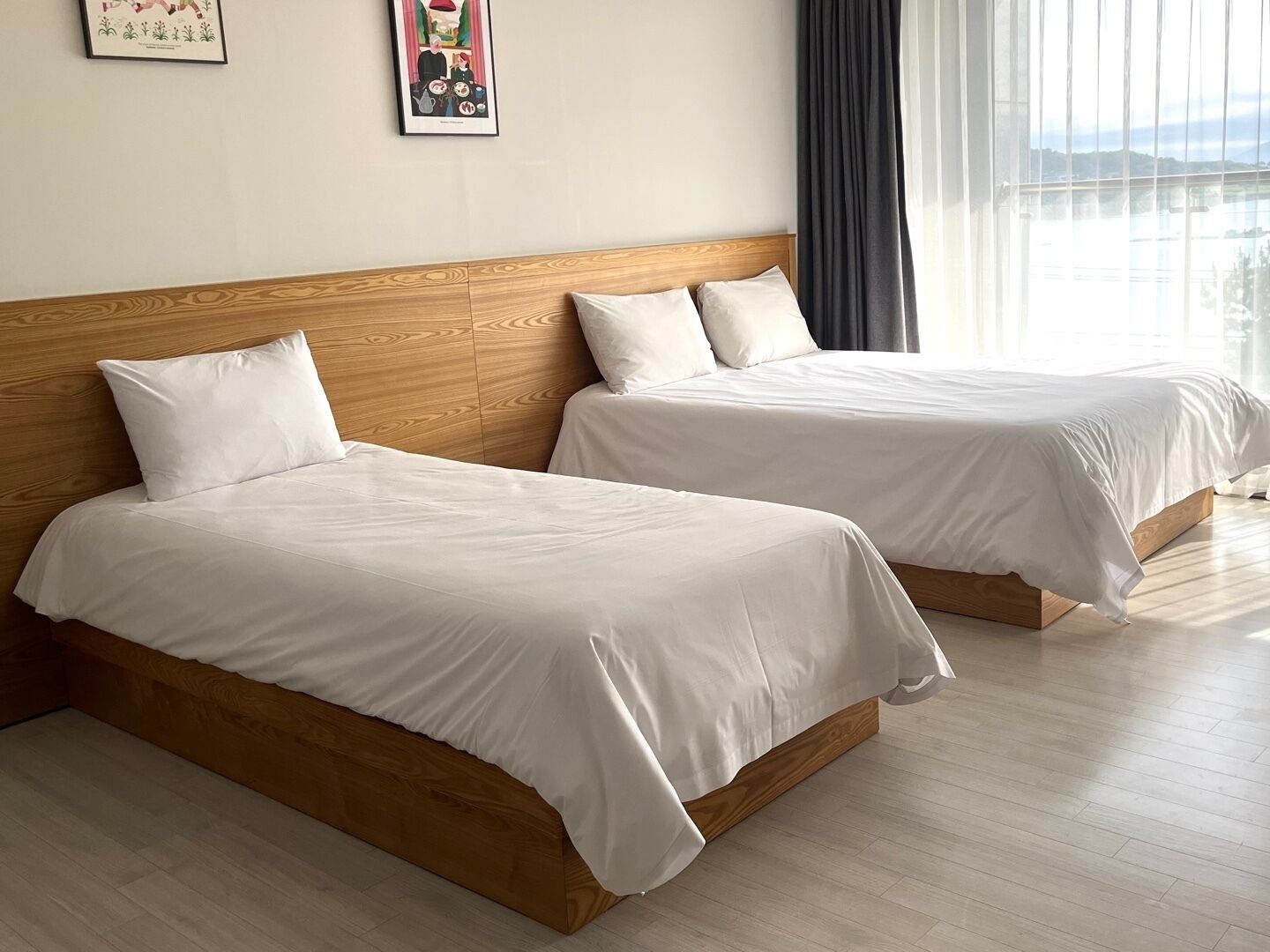 A hotel room with two beds, wooden headboards, white bedding, and a large window with curtains.