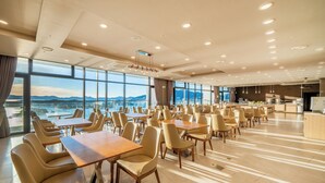 A spacious dining area with multiple tables and chairs, large windows offering a view of the mountains, and a modern ceiling design with recessed lighting. - Hotel Ocean Hill (Yeosu)
