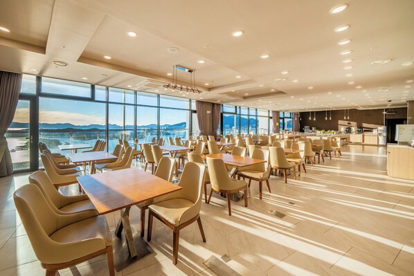 Un vaste espace dédié à la salle à manger, avec de nombreuses tables et chaises, de grandes fenêtres offrant une vue sur les montagnes et un design moderne du plafond agrémenté d’un éclairage encastré.