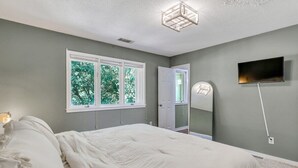 A bedroom with a bed, a TV mounted on the wall, and a window with a view of trees. - GATA 2 -The Rustic Suite - Close to GSU (Statesboro)
