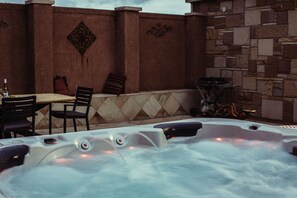 Relax in the hot tub surrounded by a serene stone wall, complete with a table and chairs for a perfect evening.