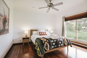 Relax in this serene bedroom with a large bed, ceiling fan, and window offering a view of the outdoors.